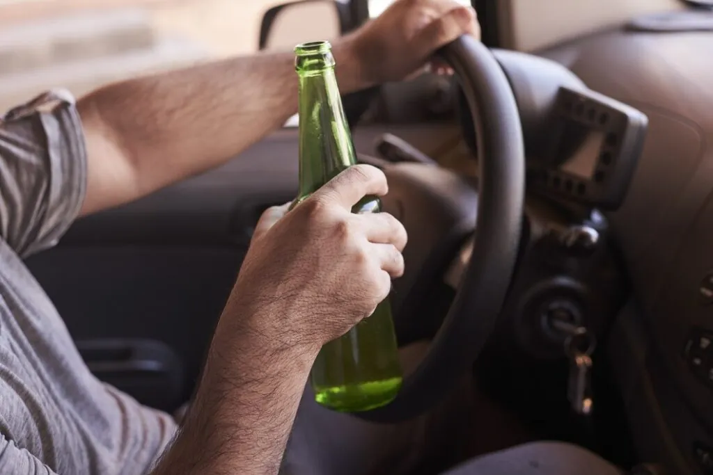 bottle-beer-man-s-hands-driving-car-daytime_181624-31614